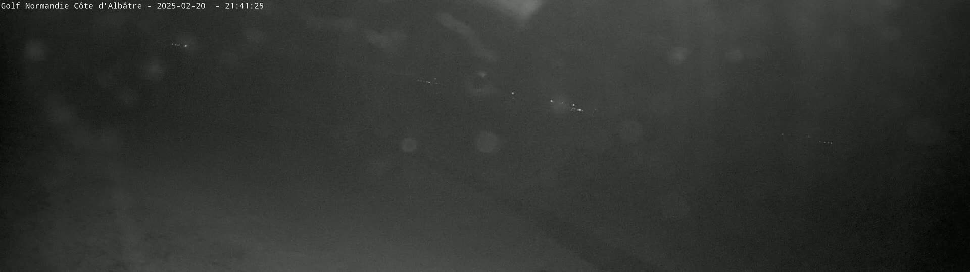 A dark, nighttime scene shows a series of faint, white lights in the distance, possibly indicating distant lights or celestial objects.