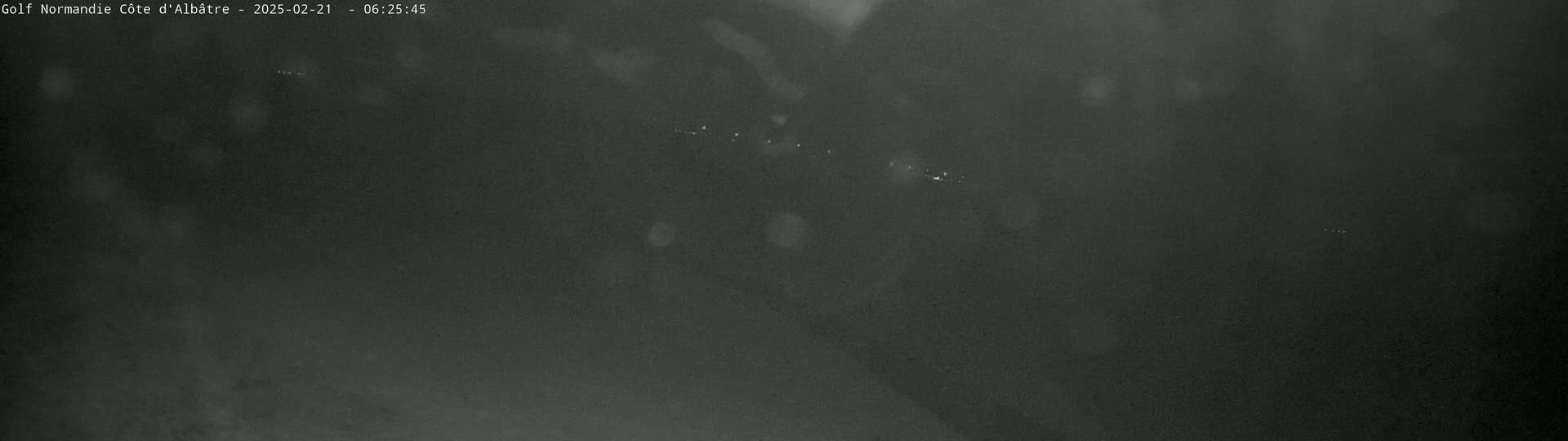 A dark, nighttime image shows a blurry view of what appears to be a road or field with faint lights in the distance.