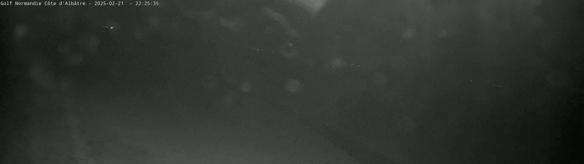 A dark, nighttime outdoor scene shows a mostly featureless, dark gray sky with a few faint, small, bright spots.