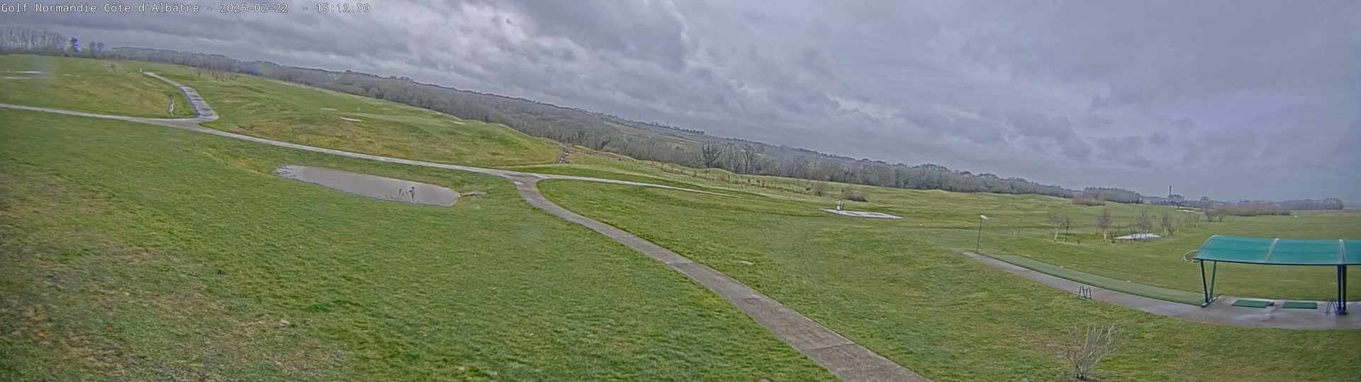 A golf course with a driving range is shown under a cloudy sky.