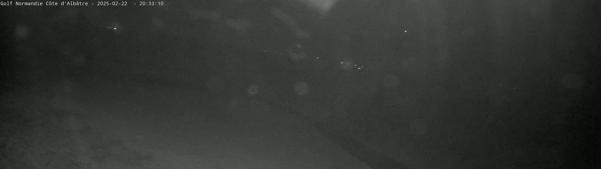 A dark, grainy image shows a nighttime scene with a few faint lights in the distance.