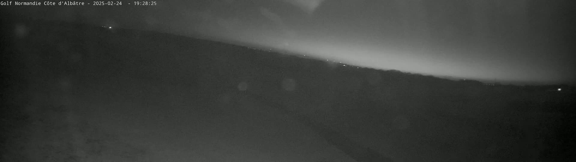 A nighttime, long shot of a dark hillside under a hazy sky with a few distant lights visible.