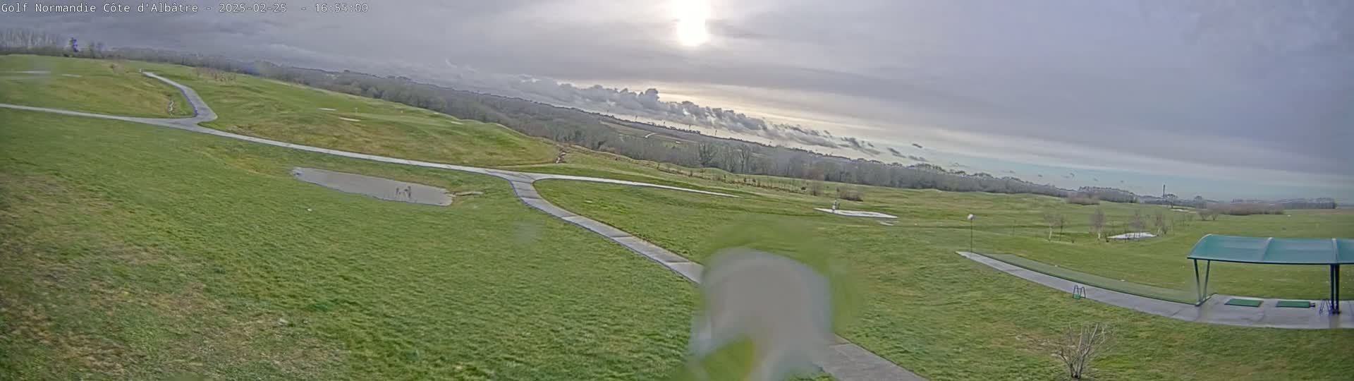A view of a golf course on an overcast day, showing fairways, walkways, and a covered driving range.