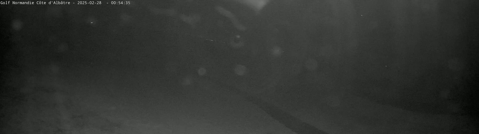 A dark, blurry nighttime outdoor scene shows a mostly featureless expanse with a few small, indistinct bright spots.