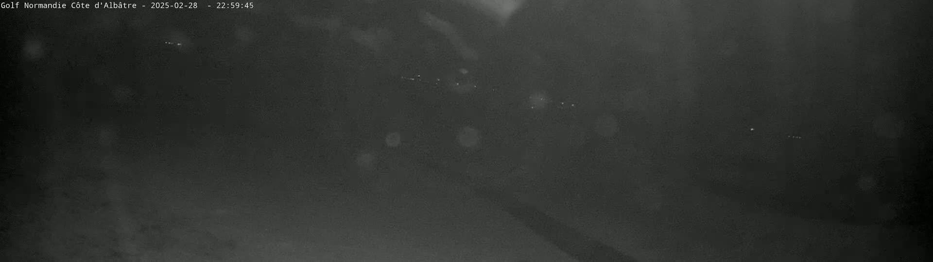 A dark, nighttime image shows a blurry, indistinct view of a landscape with a few faint lights visible in the distance.