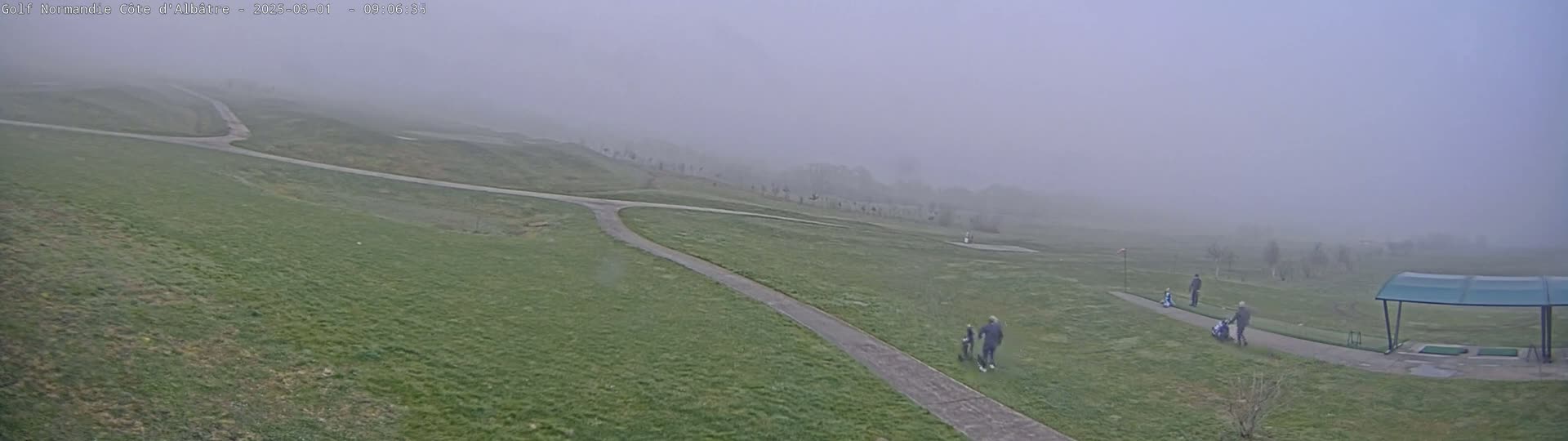 A foggy golf course with several people walking along a path.