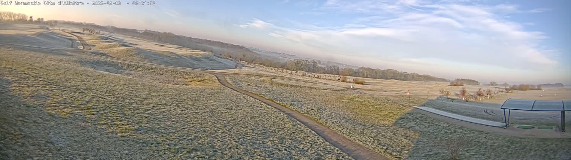 A frost-covered golf course stretches into the distance under a mostly clear, bright sky.