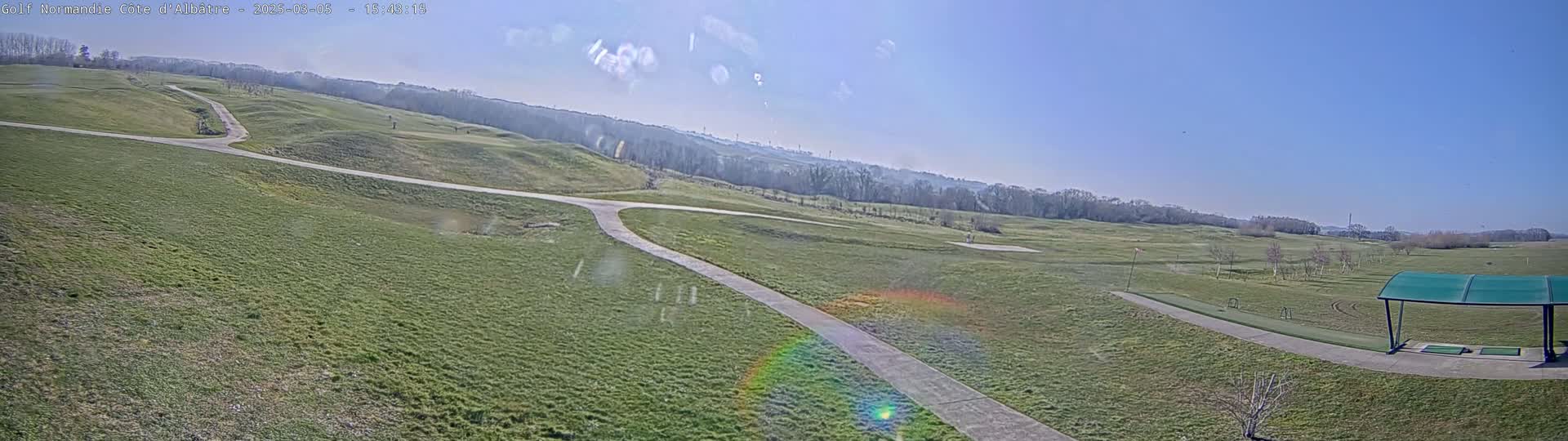 A sunny day reveals a sprawling golf course with winding pathways and a covered driving range in the foreground.