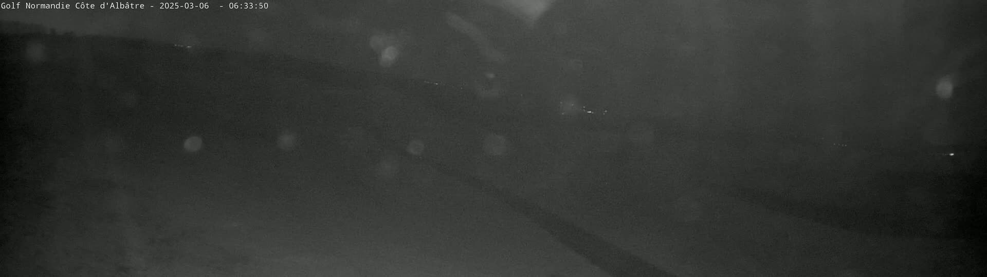 A dark, blurry nighttime image shows a landscape under rainy conditions.