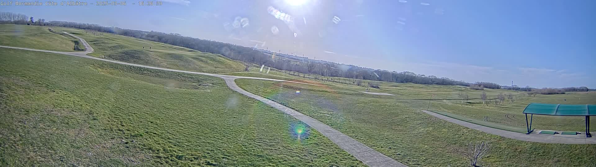 A sunny day overlooks a sprawling green golf course with winding paths and a covered driving range in the foreground.