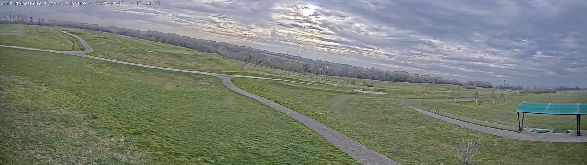 A sprawling green golf course with paved pathways stretches under a cloudy sky.