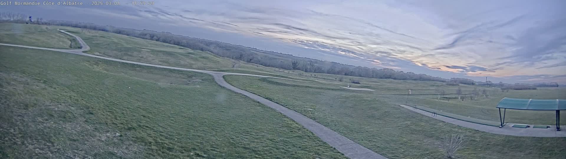 A high-angle view of a golf course with paved paths under a mostly cloudy, twilight sky.