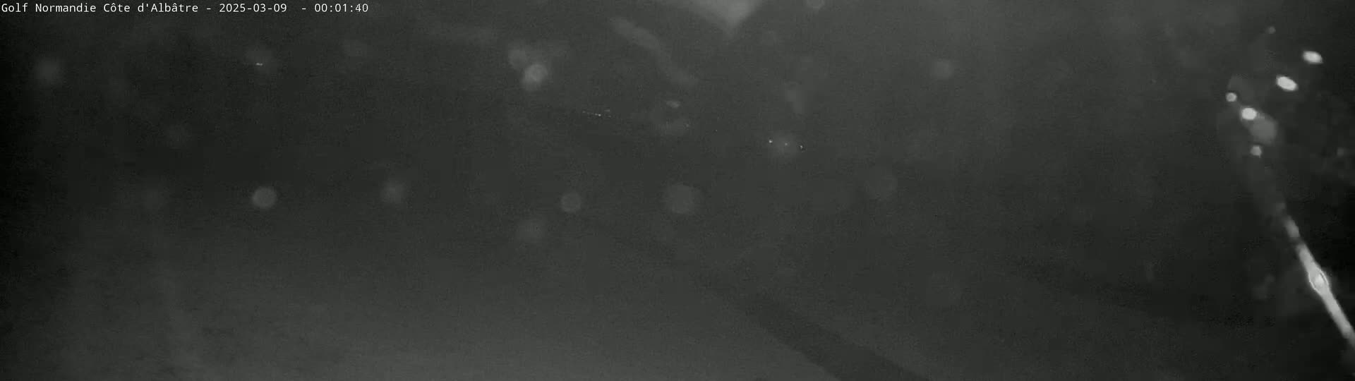 A dark, nighttime scene shows a blurry, indistinct view of what appears to be falling snow or rain.