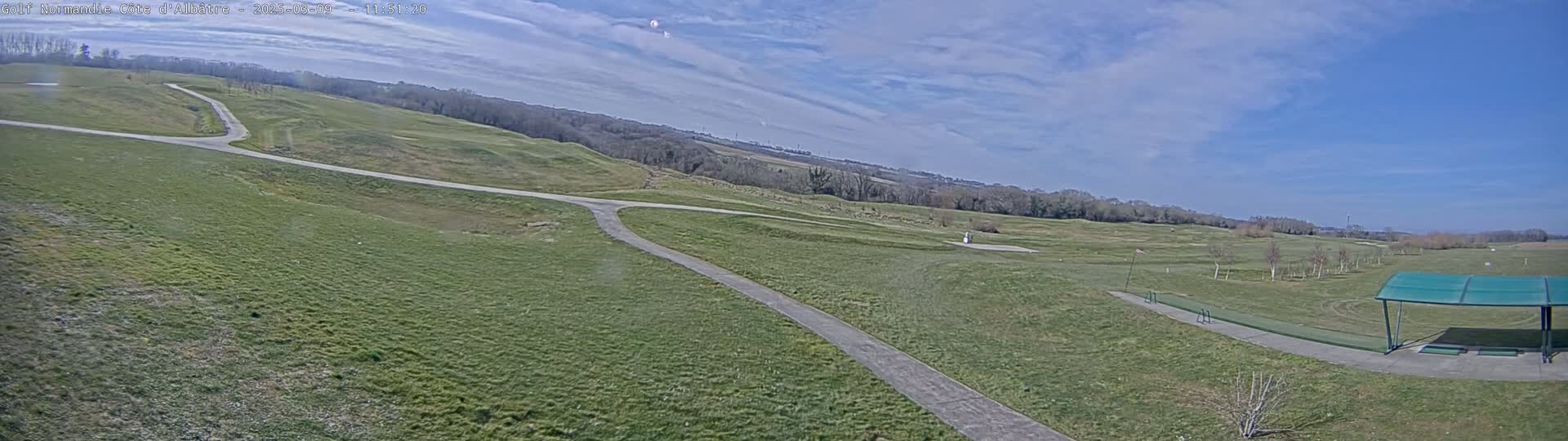 A paved path winds through a grassy golf course under a mostly sunny sky.