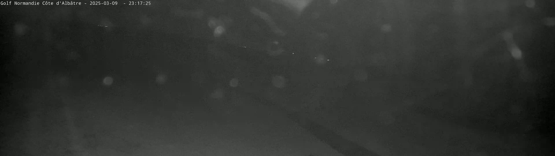 A dark, blurry nighttime scene shows rain falling in front of indistinct shapes and faint lights.
