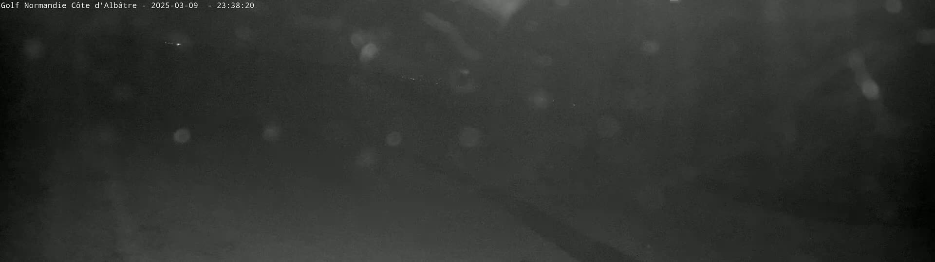 A dark, nighttime scene shows light rain or snow falling.