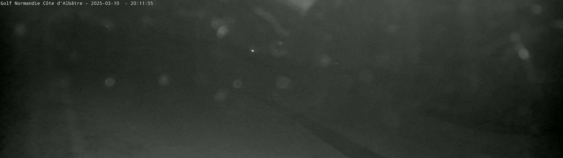 A dark, blurry nighttime image shows a few faint, indistinct lights in the distance, possibly under snowy or rainy conditions.