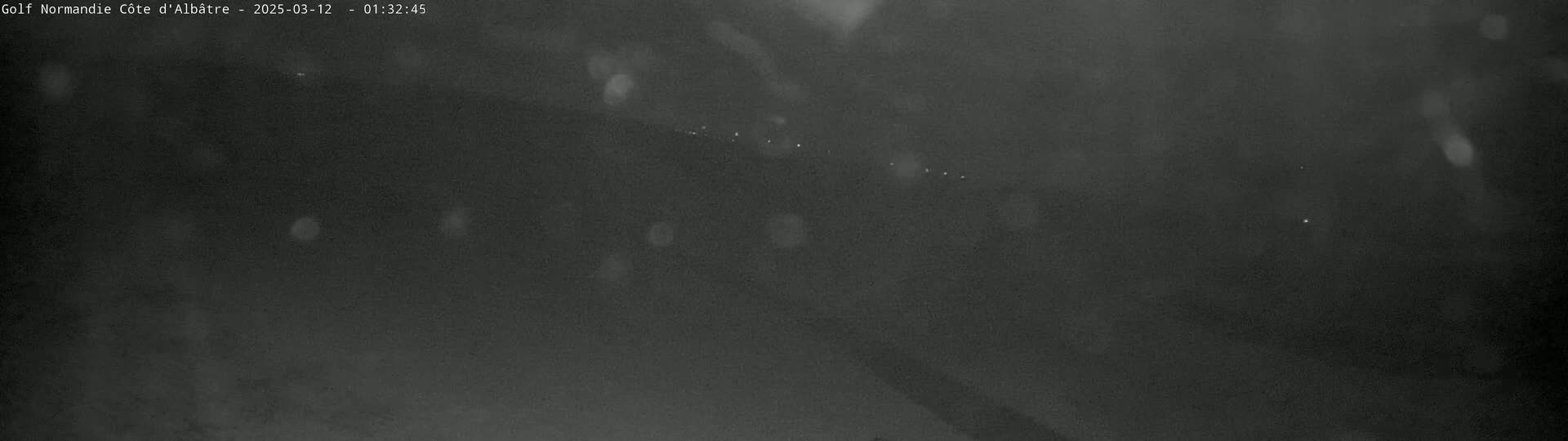 A dark, blurry nighttime scene shows a few distant lights through light rain or snow.