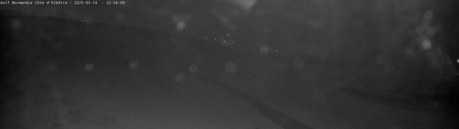 A blurry, dark nighttime image shows a faint line of lights in the distance under a rainy sky.