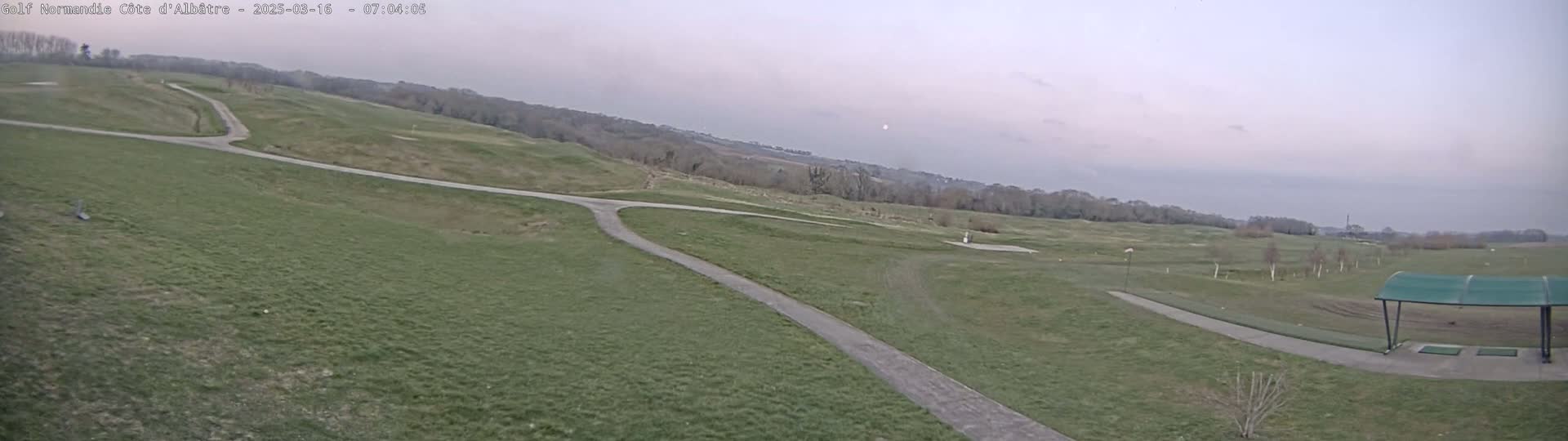 A golf course with paved paths winds through a grassy landscape under an overcast sky.