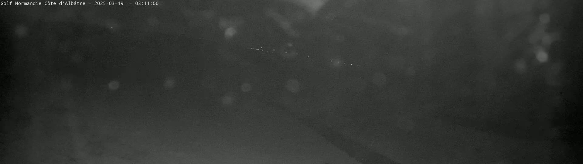 A blurry, dark nighttime image shows a few faint lights in the distance under a hazy or snowy sky.