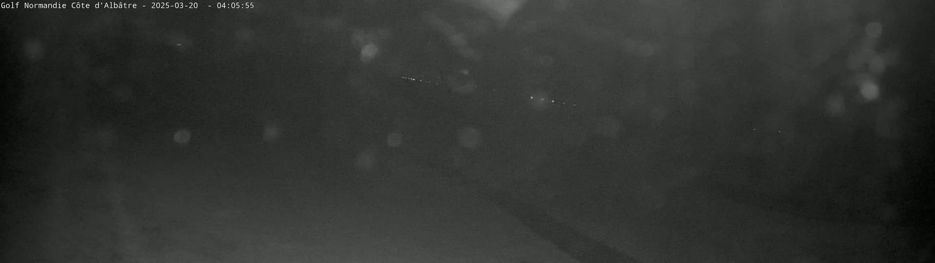A dark, blurry nighttime image shows a few faint lights in the distance, possibly from vehicles, under a seemingly clear or lightly overcast sky.