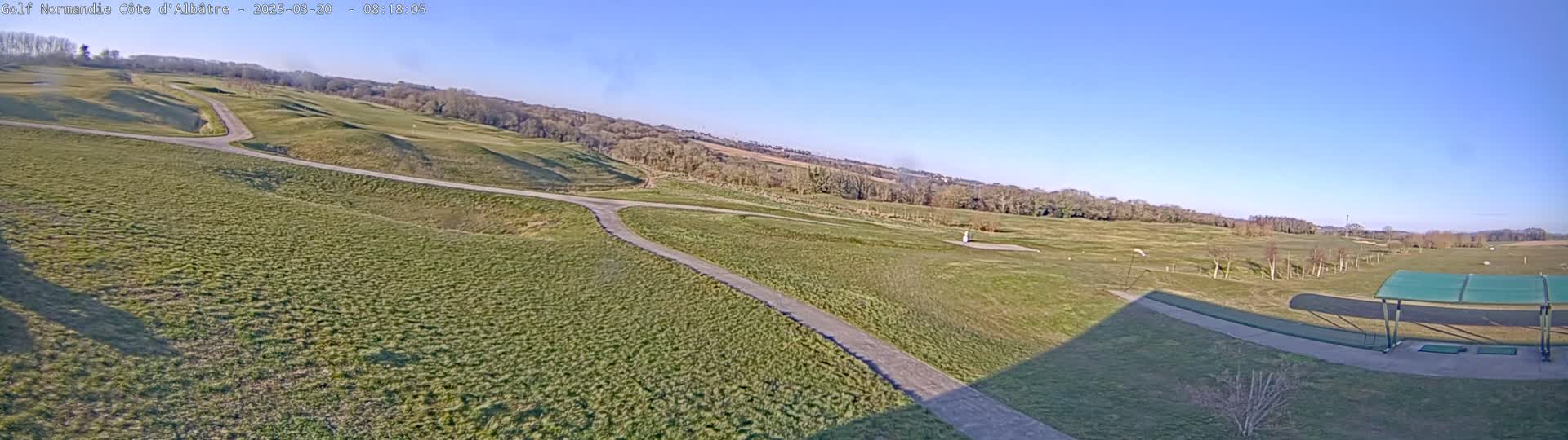 A sprawling golf course with rolling hills and a paved path under a clear, sunny sky.