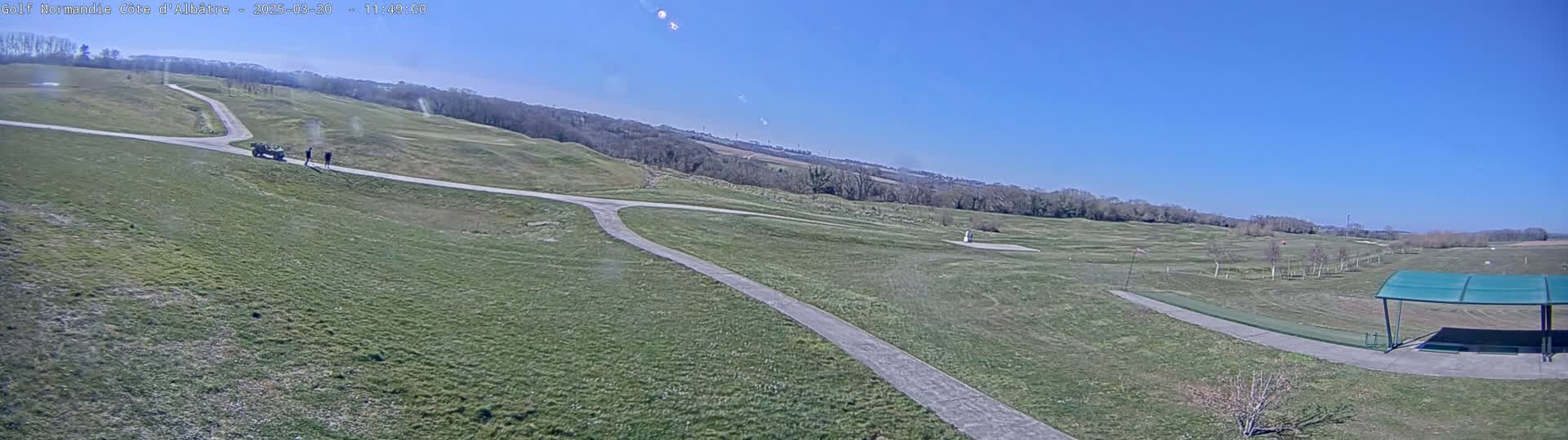 A golf course with a paved path, a few people, and a golf cart is visible under a clear, sunny sky.