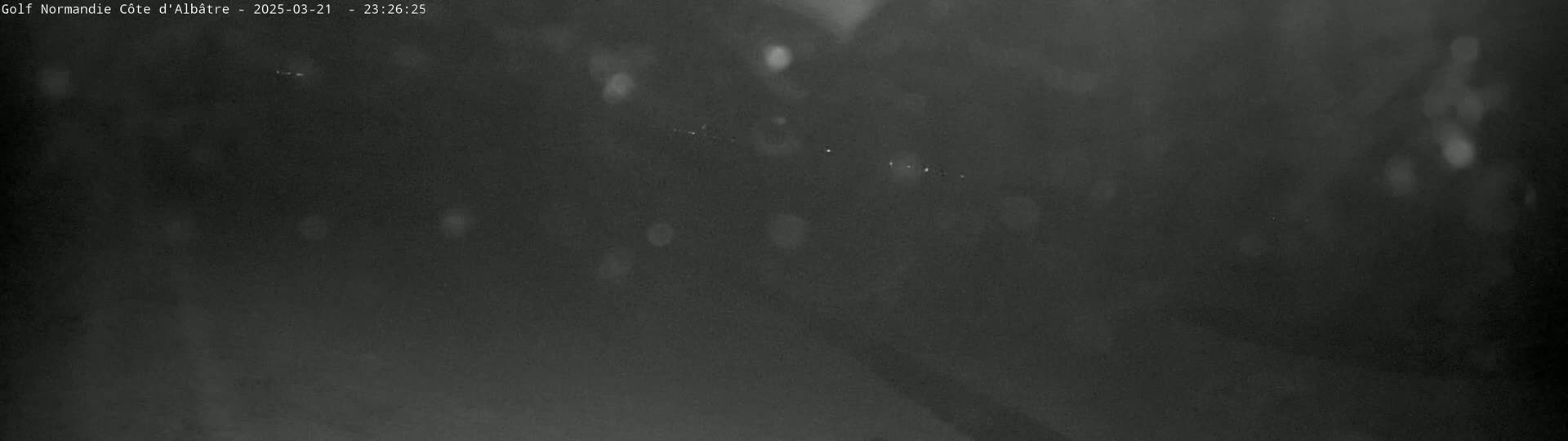 A dark, blurry nighttime outdoor scene shows a road with indistinct lights in the distance under a seemingly clear sky.