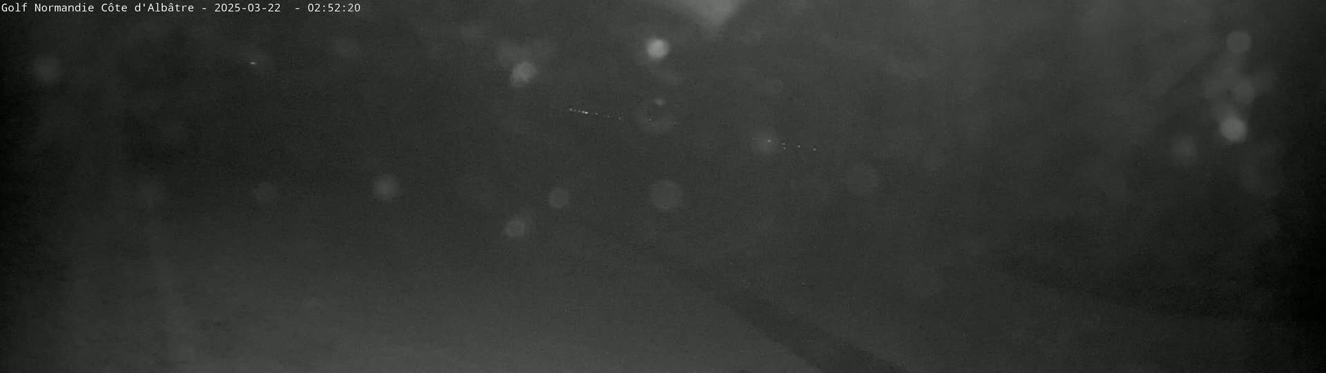 A blurry, dark nighttime scene shows a few faint lights in the distance under a possibly snowy or rainy sky.