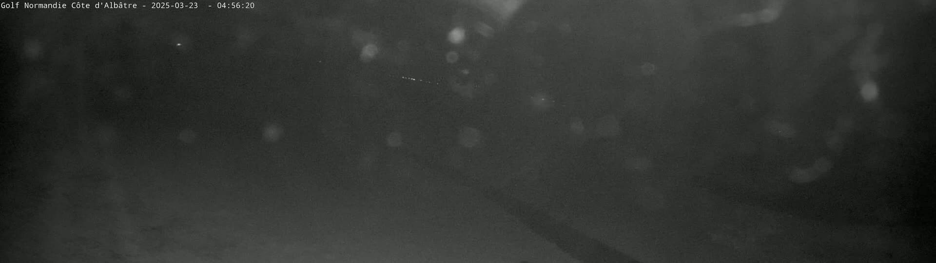 A dark, blurry nighttime scene with faint lights and what appears to be light rain or snow.