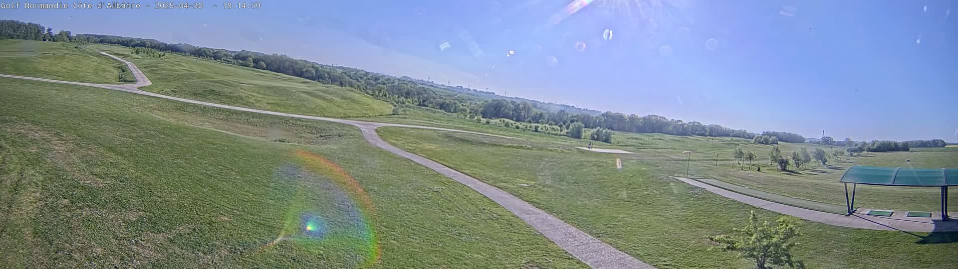 A sunny day reveals a golf course with rolling green hills, paved pathways, and a covered driving range.
