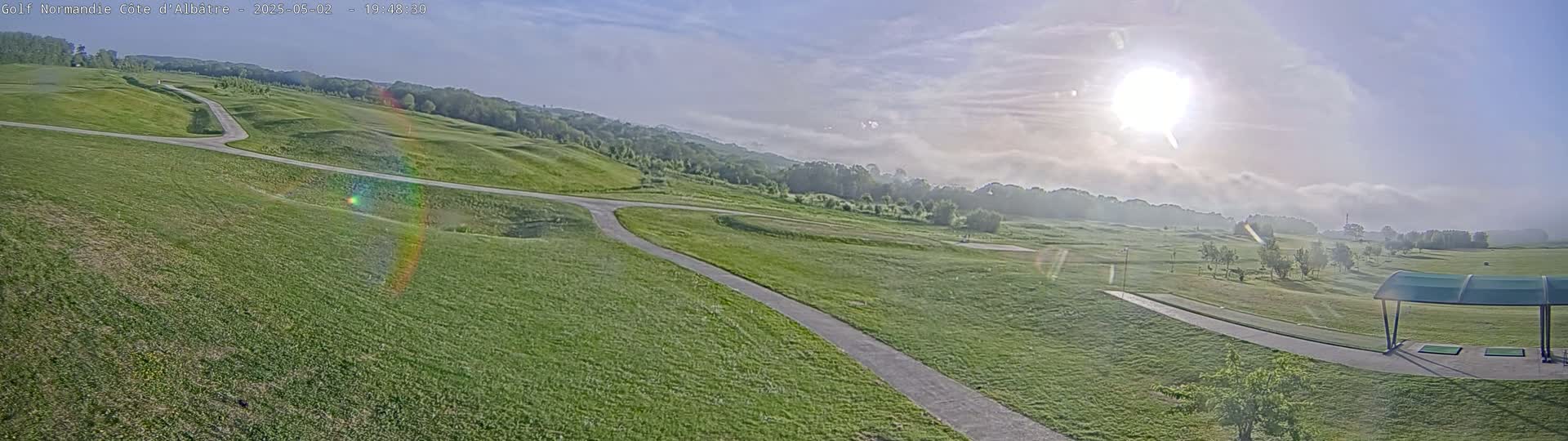 A sunny, partly foggy day overlooking a golf course with winding cart paths and a covered driving range.
