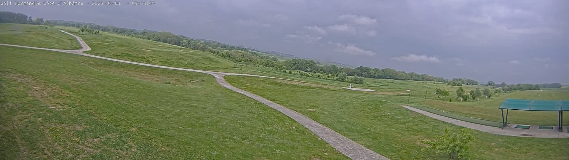 A golf course with paved pathways under a cloudy sky.