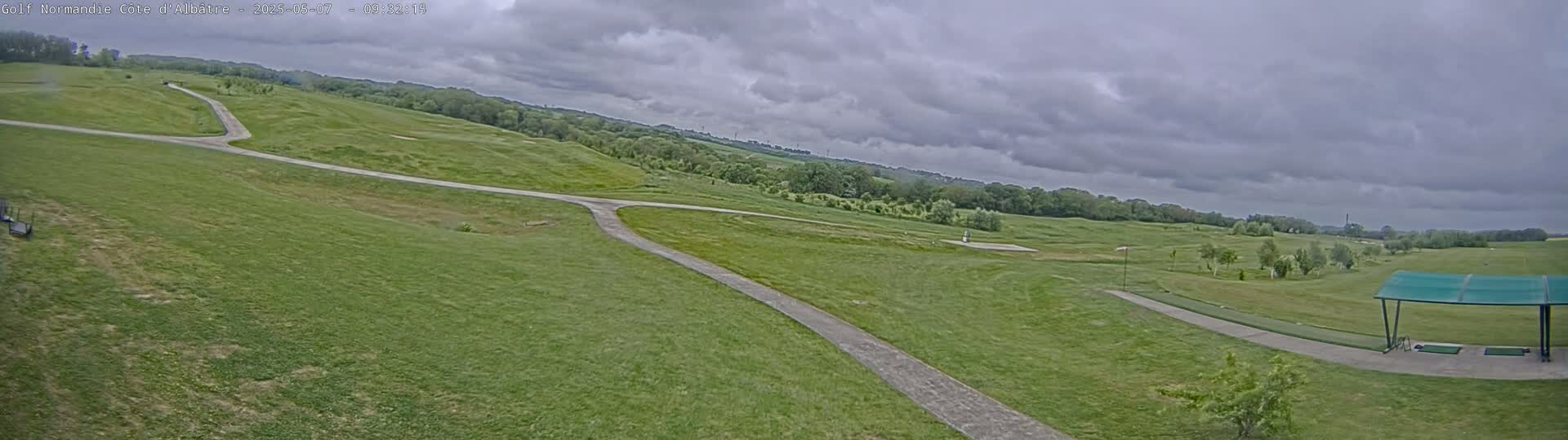A paved path winds through a grassy golf course under a cloudy sky.