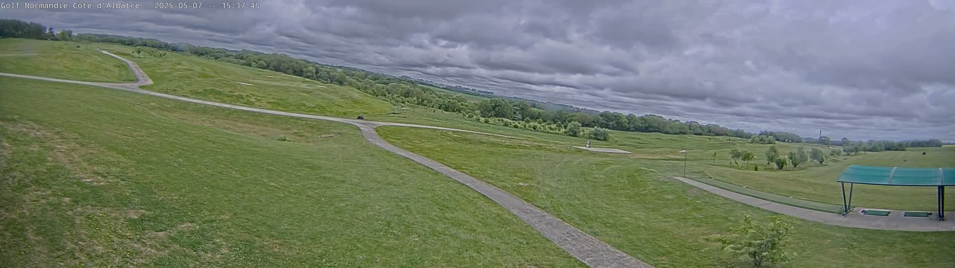 A paved path winds through a grassy golf course under a cloudy sky.