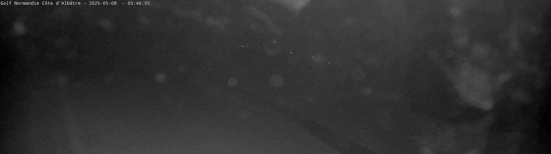 A blurry, dark image shows a distant line of faint lights at night, possibly from a town or road, under a mostly clear, dark sky.