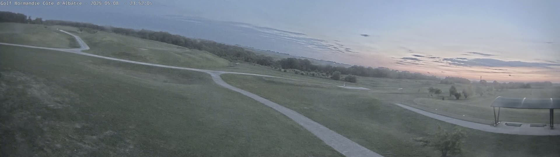 A paved path winds through a grassy golf course under a twilight sky with a pinkish hue on the horizon.