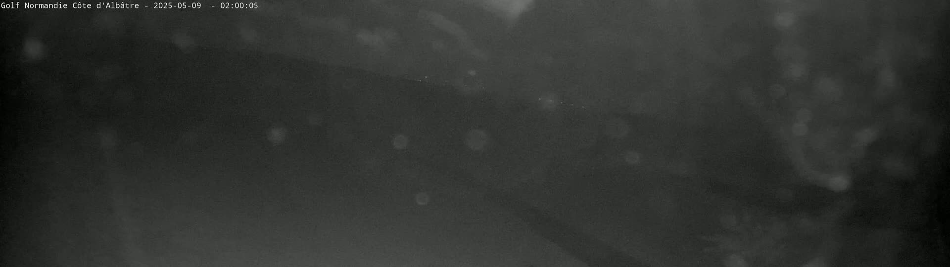 A dark, blurry image shows a nighttime outdoor scene with light rain or snow falling.
