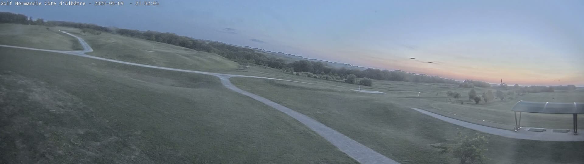 A high-angle view shows a golf course with paved paths at sunset under a mostly clear sky.