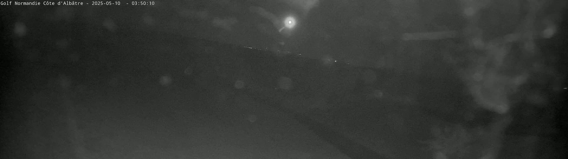 A nighttime, blurry outdoor image shows a dark landscape under a hazy sky with a bright light source visible in the distance.