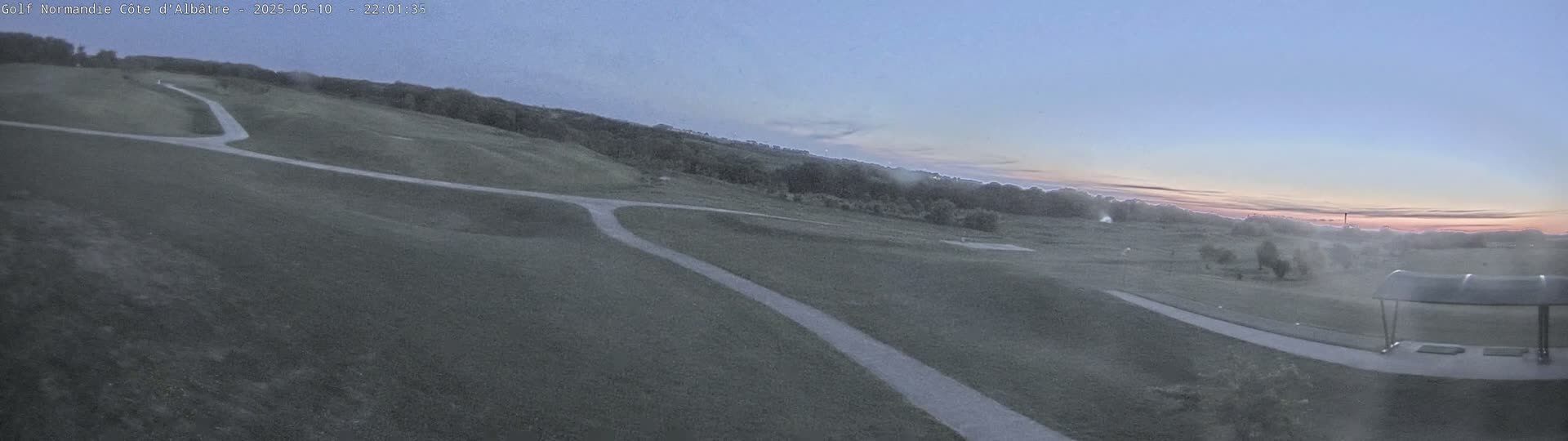 A wide, elevated view of a golf course with winding paths at dusk, under a clear, pale sky.
