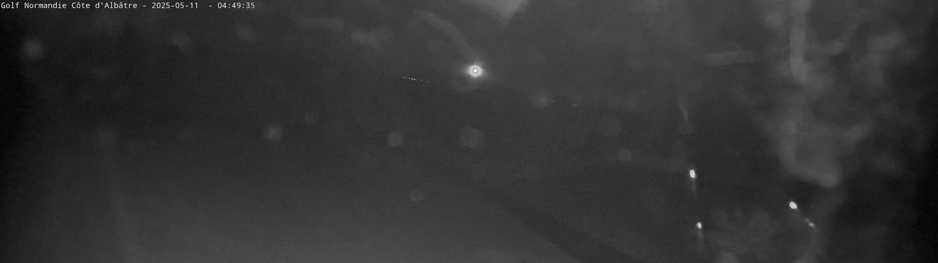 A nighttime, low-light image shows a dark, blurry scene with a few distant bright lights.