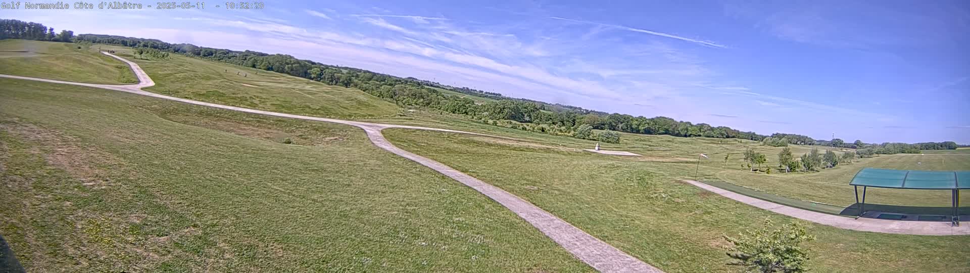 A paved path winds through a grassy golf course under a mostly clear, sunny sky.