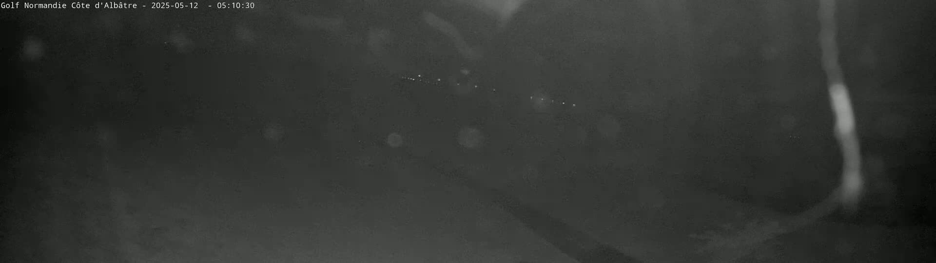 A low-light, nighttime image shows a blurry view of a line of lights in the distance.