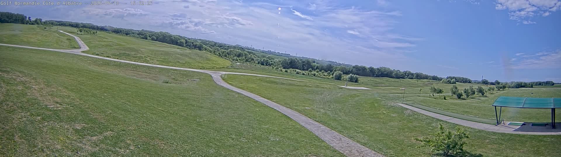 A mostly sunny day reveals a golf course with winding cart paths, green fairways, and a covered driving range in the lower right.