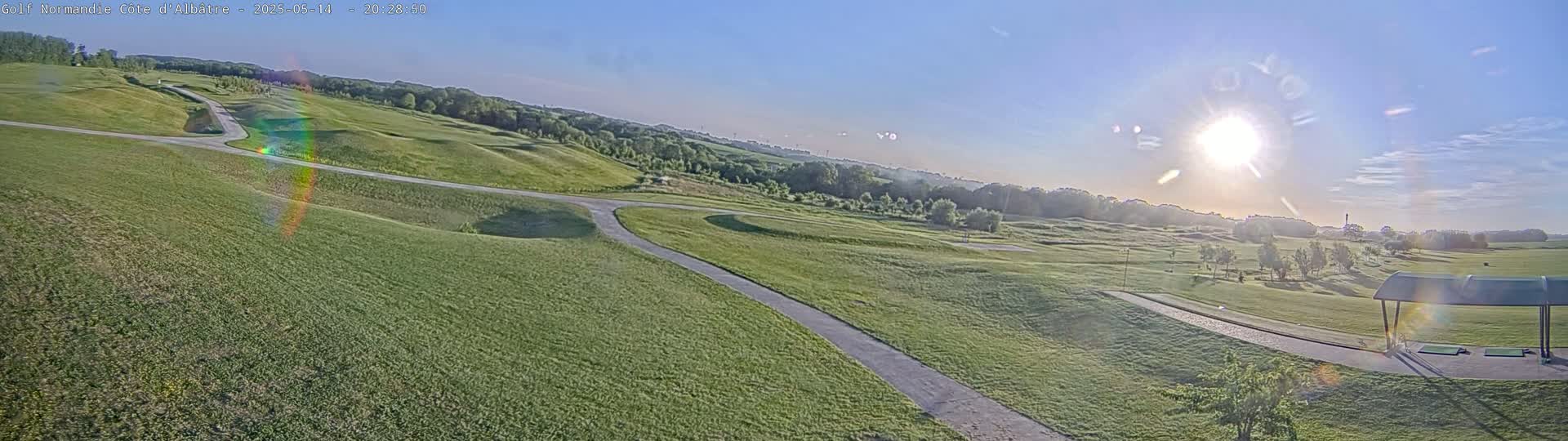 A sunny day reveals a sprawling golf course with rolling green hills, winding paths, and a covered driving range.