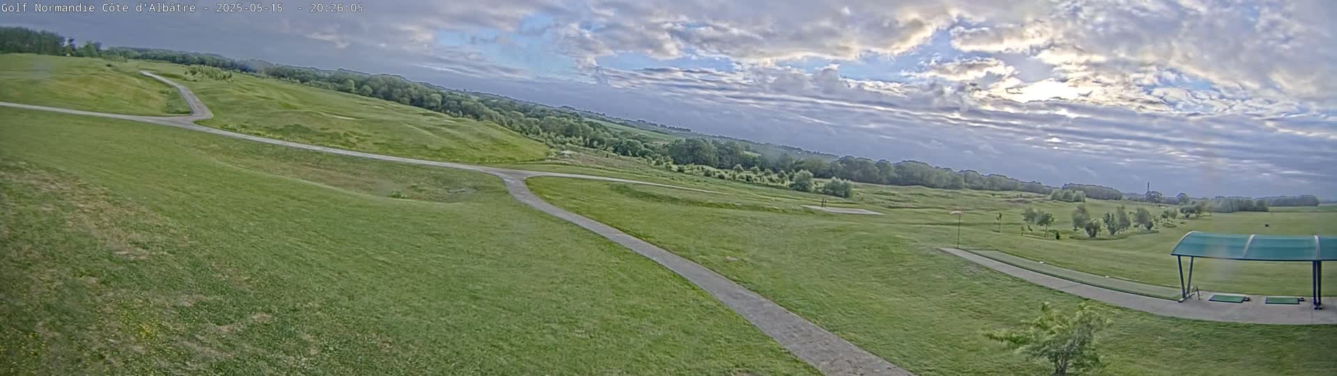 A mostly sunny, partly cloudy day reveals a golf course with winding paths and a covered driving range.