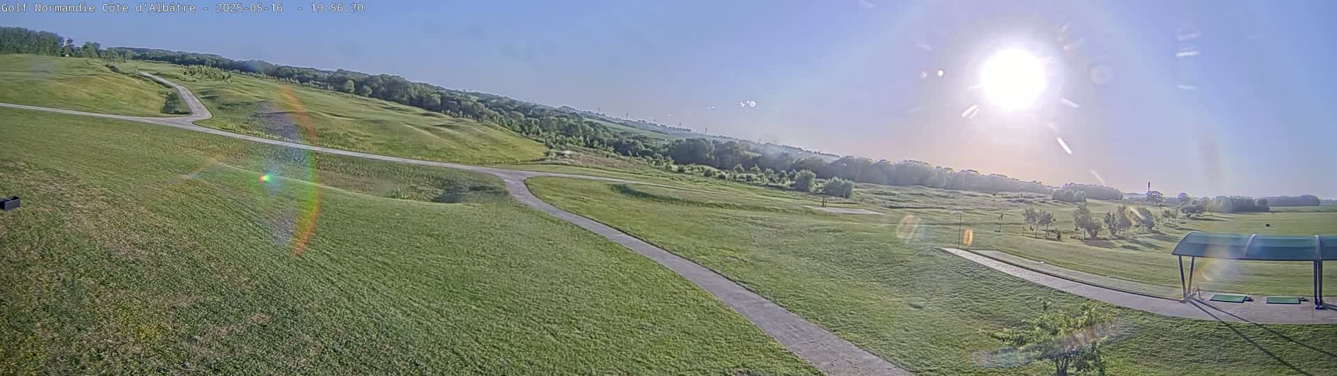 A sunny day reveals a sprawling green golf course with winding cart paths, and a covered driving range in the foreground.