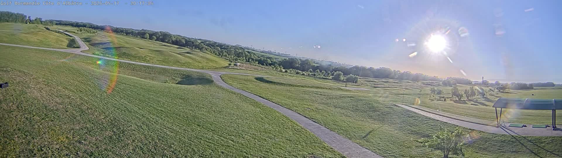 A sunny day reveals a sprawling golf course with rolling green hills, paved pathways, and a covered driving range.